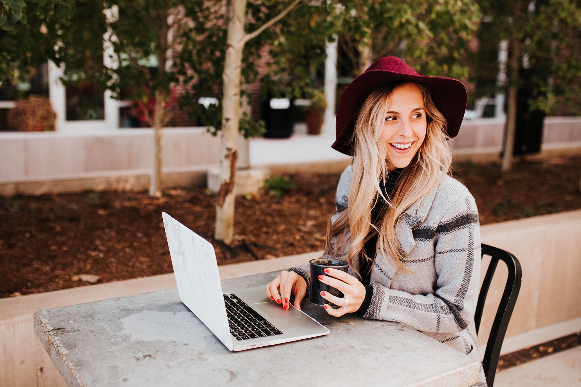 Woman sitting at computer outside with coffee.