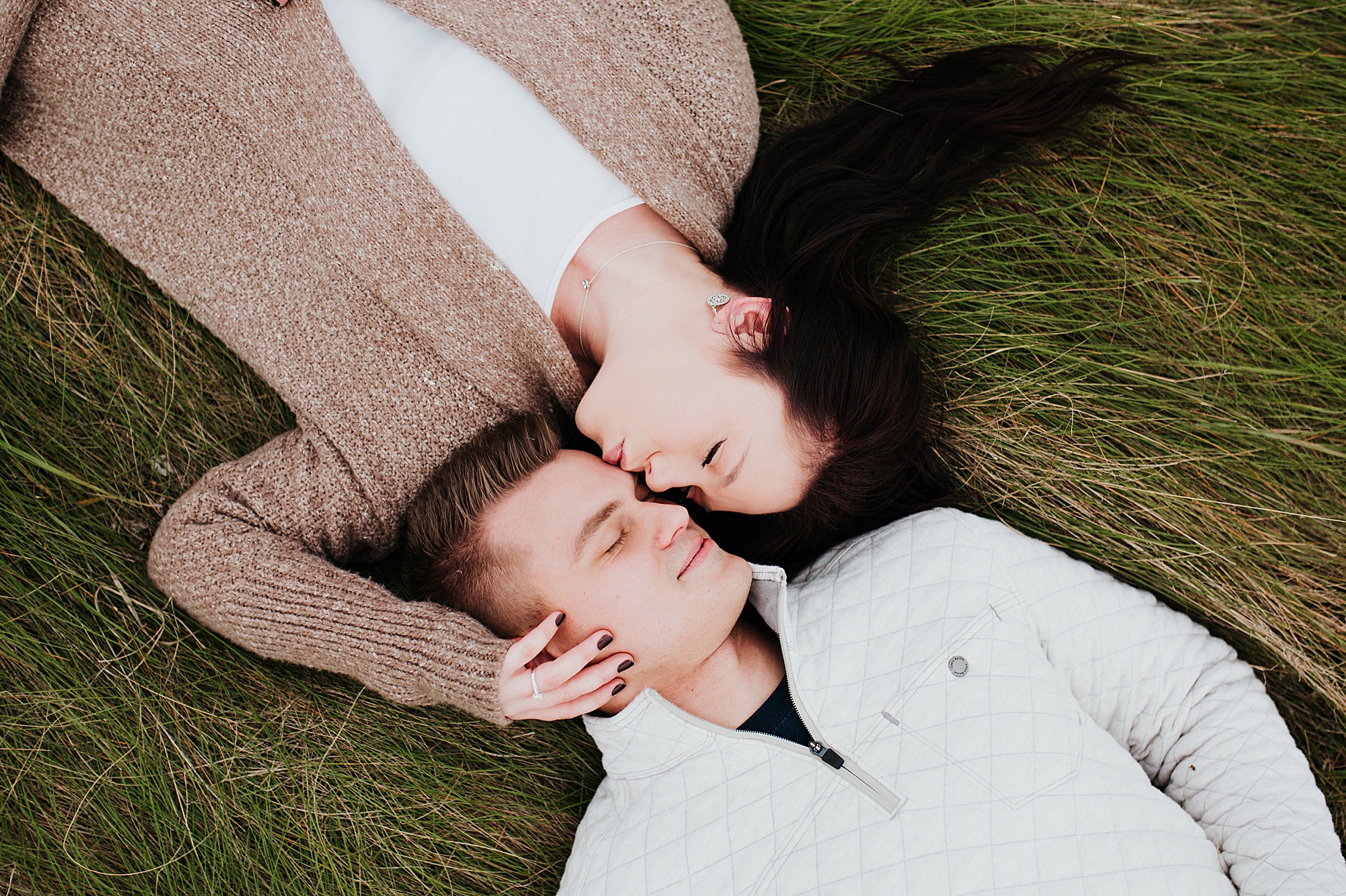engaged couple laying in the grass.